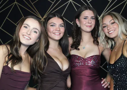 Four friends in ball gowns posing in front of a black and gold backdrop