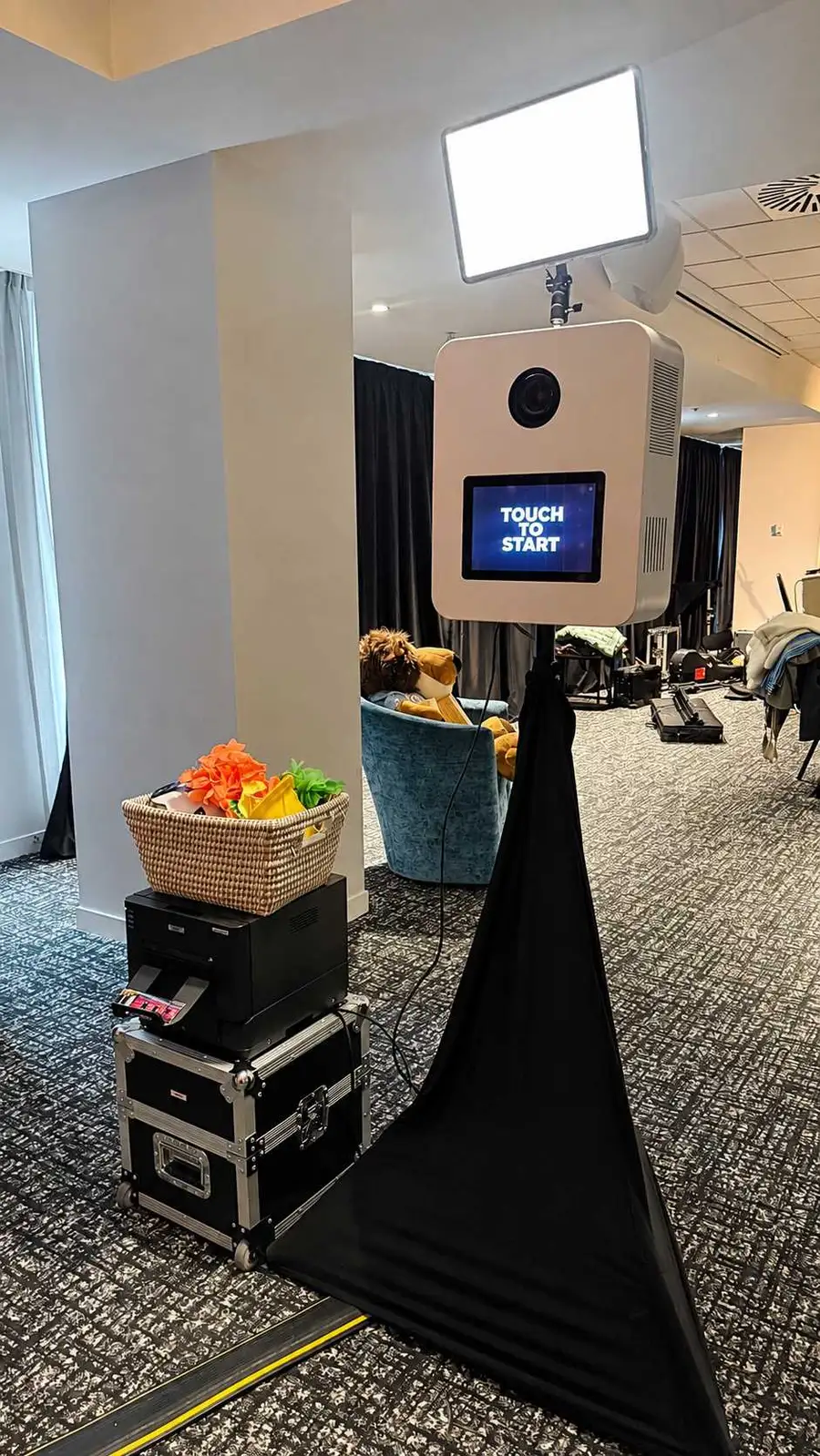 Snapic booth with a rectangular light, touch screen and black draped stand beside a printer and props