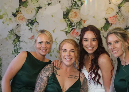 A bride and bridesmaids posing in front of a flower wall